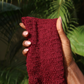 Hand holding an authentic exfoliating net sponge against a green leafy background