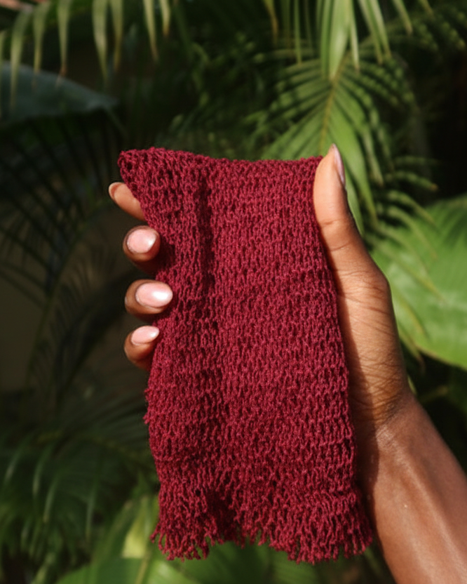 Hand holding an authentic exfoliating net sponge against a green leafy background